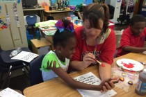 Mia Rotondo works on an art project with a student. They're dressed up for 80s Day at Ben Franklin Elementary. Credit: Mallory Falk/WWNO.